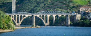 Douro nehri boyunca uzanan yüksek açılı iki köprüden yüksek açılı görüntü tepenin altındaki üzüm bağları terasları, açık gökyüzü altında peso da regua, Portekiz 