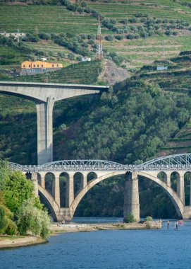 Douro nehri boyunca uzanan yüksek açılı iki köprüden yüksek açılı görüntü tepenin altındaki üzüm bağları terasları, açık gökyüzü altında peso da regua, Portekiz 