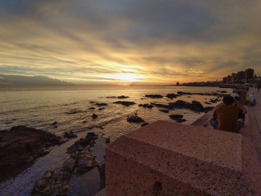 Gün batımında Montevideo sahilinin geniş bir görüntüsü. Sıcak ışık suya ve ufka yansıyor. Huzurlu ve huzurlu bir manzara yaratıyor.