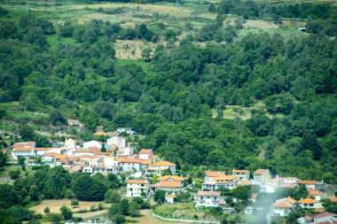 A high angle view of a traditional Portuguese village with white houses and red roofs, nestled in a lush, forested green valley. 