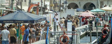 Aveiro, Portugal: August 15 2023: High angle view of a crowded canal area in Aveiro Portugal with people walking near traditional boats and market stalls