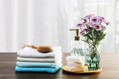 Açık mavi havlular, sabun, çiçekler ve ahşap arka planda banyo süslemeleri..