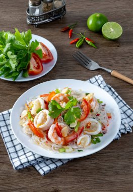 Ahşap bir masada cam erişte deniz ürünleri salatası.
