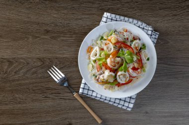 Ahşap bir masada cam erişte deniz ürünleri salatası.