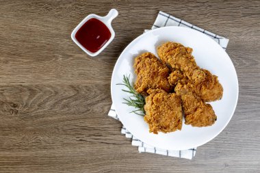 Tahta masadaki domates soslu beyaz tabakta kızarmış tavuk.
