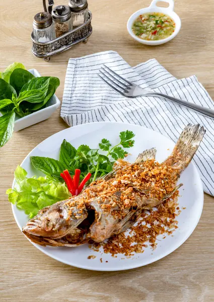 Kızarmış deniz levreği Çin sarımsağı serpiştirilmiş. Beyaz bir tabakta, masanın üzerinde kızarana kadar kızartılmış.. 