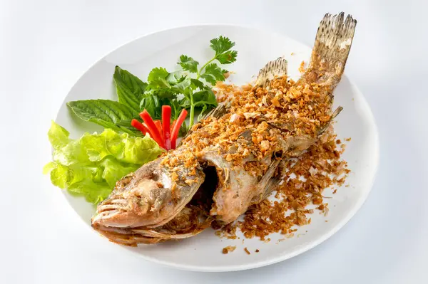 Kızarmış deniz levreği Çin sarımsağı serpiştirilmiş. Beyaz bir tabakta, masanın üzerinde kızarana kadar kızartılmış.. 
