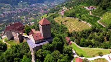 İtalyan ortaçağ kaleleri - Merano 'daki görkemli Tirolo Kalesi. Alp dağları ve üzüm bağlarıyla çevrili. Bolzano bölgesi, İtalya. Hava aracı üstten uçuyor.