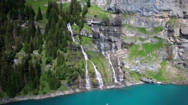 Idyllic İsviçre 'nin Oeschinensee dağı (Oeschinen) şelalesi ve Kandersteg kasabası yakınlarındaki Alp dağlarının karlı zirveleriyle. Hava aracı panoramik video 4K. İsviçre doğa manzarası