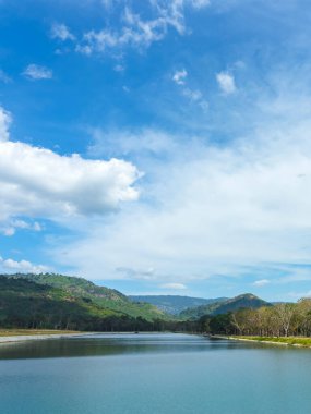 Etrafı dağlarla çevrili güzel ve huzurlu bir göl ve güzel güneş ışığı ve Tayland 'da bulutlu bir gökyüzü. Huzurlu ve güzel doğal bir göl manzarası..