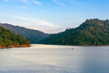 Yeşil ormanlı mavi nehirde yüzen uzun kuyruklu teknenin görüntüsü. Nehir Tayland 'da Khun Dan Prakan Chon Barajı' nda. Manzara. Akşamları manzaranın tadını çıkarmak için tekneye binen turistler. Turizm konsepti