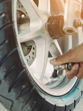 Adamın elleri enflasyon basıncını ölçer ve motorun lastiğini hava kompresörüyle şişirir. Adam hava basıncını kontrol ediyor ve otomatik hava doldurucudan motosiklet tekerindeki lastik basıncını dolduruyor..