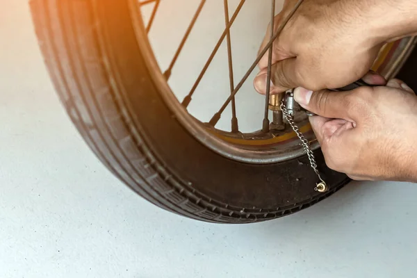 Hands of man check inflator pressure and inflates tire on motorcycle with bicycle floor pump. Man checking air pressure and filling the tire pressure on the motorbike wheel from pressurized air pump.