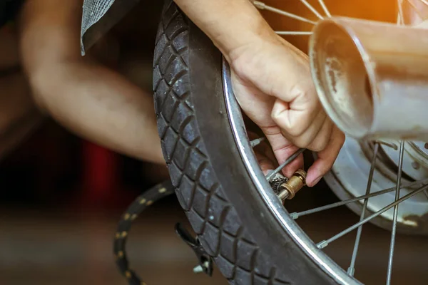 Hands of man check inflator pressure and inflates tire on motorcycle with bicycle floor pump. Man checking air pressure and filling the tire pressure on the motorbike wheel from pressurized air pump.