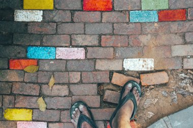 İnsanın ayakları, eski güzel çok renkli tuğlaların üzerinde sandalet giyer tuğla dokusu ya da soyut taş kaldırım arka planı gibi kaldırımda taş döşeme deseni oluşturur. Arkaplan ve doku.