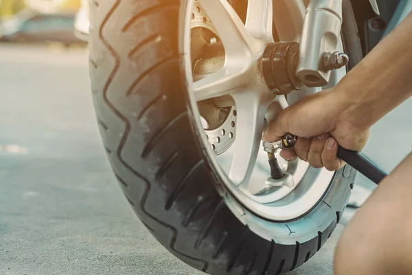 Hands of man check inflator pressure and inflates a tire on motorcycle with an air compressor. Man checking air pressure and filling the tire pressure on the motorbike wheel from automatic air filler.