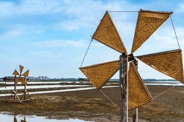 Wooden turbine at salt pan using for press seawater up to field with blue sky background in summer time of Thailand,South East Asia. Beautiful landscape of salt fields.Traditional salt farming culture