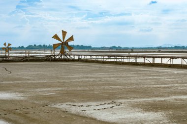Wooden turbine at salt pan using for press seawater up to field with blue sky background in summer time of Thailand,South East Asia. Beautiful landscape of salt fields.Traditional salt farming culture