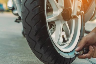 Adamın elleri enflasyon basıncını ölçer ve motorun lastiğini hava kompresörüyle şişirir. Adam hava basıncını kontrol ediyor ve otomatik hava doldurucudan motosiklet tekerindeki lastik basıncını dolduruyor..
