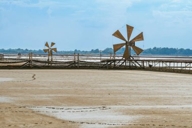 Wooden turbine at salt pan using for press seawater up to field with blue sky background in summer time of Thailand,South East Asia. Beautiful landscape of salt fields.Traditional salt farming culture