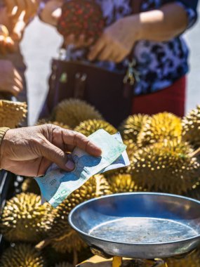 Yaşlı Taylandlı kadın satıcı yol kenarındaki turistlere durian, meyve ve sebze satarak motosiklet sürüyor. Sokak tüccarı taze Durian eti kesip satmış. Durian ticareti. Seçici odak.