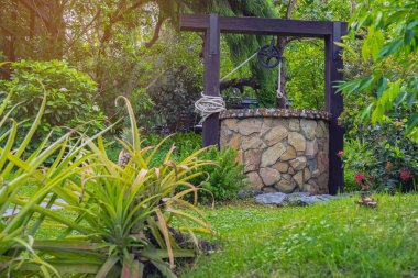 Taş ve tekerlek makara ile yapılmış güzel artezyen metal kova ve halatla huzurlu bahçe atmosferinde. Kırsal alandaki Retro Stone Kuyusu. Antika eşyalarla güzel bir bahçe dekorasyonu..