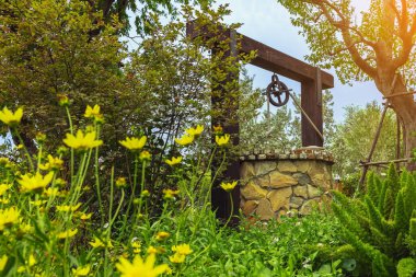 Taş ve tekerlek makara ile yapılmış güzel artezyen metal kova ve halatla huzurlu bahçe atmosferinde. Kırsal alandaki Retro Stone Kuyusu. Antika eşyalarla güzel bir bahçe dekorasyonu..