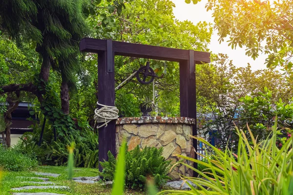 Beautiful artesian well made by stones and wheel pulley with metal bucket and rope in peaceful garden atmosphere. Retro stone water well in rural area. Beautiful garden decoration with antique items.