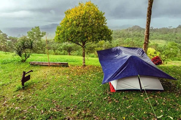 stock image Camping activities in rain-filled holiday. Tent on campsite by the hill in rainy day. Tent wet after rain. Water droplets on the tent. Raindrops on a tourist tent. Mountain camp in forest in the rain.