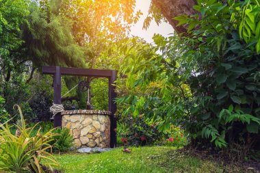 Taş ve tekerlek makara ile yapılmış güzel artezyen metal kova ve halatla huzurlu bahçe atmosferinde. Kırsal alandaki Retro Stone Kuyusu. Antika eşyalarla güzel bir bahçe dekorasyonu..