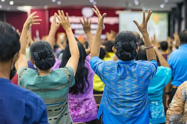 stock image Back view of senior women hands raised to workout and exercise rhythmic activities in the auditorium. Asian elderly active participants in conference room. Joyful listeners of business conference.