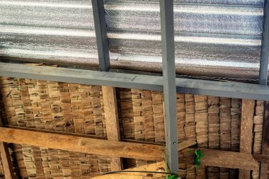 Tavan yalıtımla kaplı ve sazdan çatıyla birleştirilmiş. Alüminyum folyo ısı radyasyonunu yansıtmak için çatı altına yerleştirildi. Tavan arası yalıtımı. Karışık malzeme yapısının çatı yüzeyi detayı.