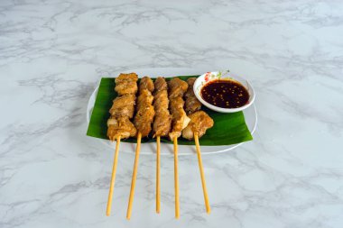 Tayland baharatlı soslu ızgara timsah bifteği mi yoksa mermer arka planda muz yaprağının üzerinde Jaew sosu mu? Barbekü soslu timsah. Masadaki beyaz tabakta kızarmış timsah eti..