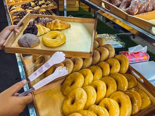 Woman buying donuts in baking store. Female choosing and buying fresh tasty pastry from shelves. Young woman choose freshly baked donuts in street food bakery. Customer buy doughnut. Selective focus.