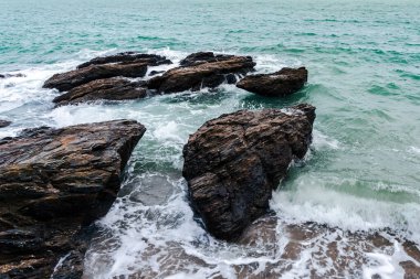 Deniz kıyısındaki kayalara vuran dalgaların üst görüntüsü, oldukça sakin bir deniz. Tayland körfezinin kayalık kıyılarında dalgalar çarpıyor. Doğu kıyısının deniz manzarası. Fırtına dalgası iskeledeki taşları kırıyor..
