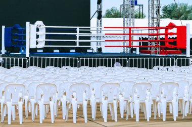 Boxing ring and many chairs for spectators prepared for competition, Outdoors. Sport and empty boxing ring in the city for a wrestling competition for athletes or boxers. Boxing ring with white seats. clipart