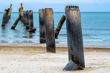 Eski iskelenin yaslanmış sütunlarının güzel manzarası. Eğik beton kutup plajı. Terk edilmiş balıkçı iskelesi, deniz kenarında. Birçok eski beton sütun deniz tarafından sahile bırakıldı. Seçici odak.