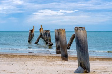 Eski iskelenin yaslanmış sütunlarının güzel manzarası. Eğik beton kutup plajı. Terk edilmiş balıkçı iskelesi, deniz kenarında. Birçok eski beton sütun deniz tarafından sahile bırakıldı. Seçici odak.