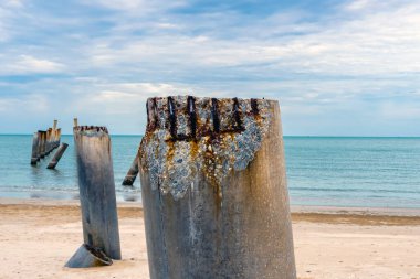Eski iskelenin yaslanmış sütunlarının güzel manzarası. Eğik beton kutup plajı. Terk edilmiş balıkçı iskelesi, deniz kenarında. Birçok eski beton sütun deniz tarafından sahile bırakıldı. Seçici odak.