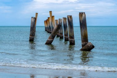 Eski iskelenin yaslanmış sütunlarının güzel manzarası. Eğik beton kutup plajı. Terk edilmiş balıkçı iskelesi, deniz kenarında. Birçok eski beton sütun deniz tarafından sahile bırakıldı. Seçici odak.