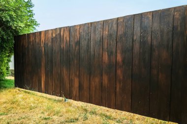 Kahverengi ahşap ahşap duvar dokusu. Bahçedeki meşe ağacından çitlerin yüzeyi. Yeşil çimleri ve ağaçları olan ahşap çitler. Eski ahşap panelin güzel koyu desenli, ahşap duvar dokusu var..