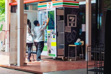 KANCHANABURI, THAILAND - 4 Ekim 2020: Kimliği belirsiz iki Asyalı kadın teneke kutuyu, içecek ve atıştırmalıkları 7-11 otomatına doldurup PTT benzin istasyonunda eksiksiz olup olmadığını kontrol edin.