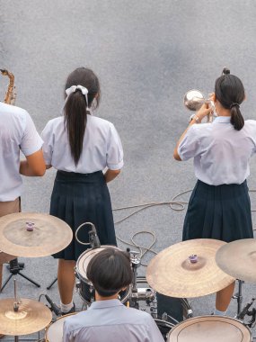 Bir grup Asyalı üniformalı öğrenci stadyumda festival orkestrası performansı sergiliyorlar. Öğrenciler kutlamalarda bando oynuyorlar. Öğrenci müzik grubu Jazz Müzik çalıyor. Eğitim açık havada.