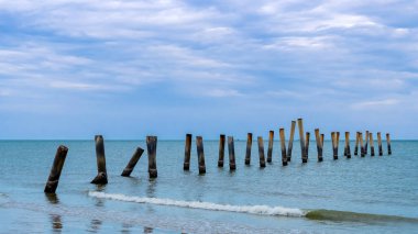 Eski iskelenin yaslanmış sütunlarının güzel manzarası. Eğik beton kutup plajı. Terk edilmiş balıkçı iskelesi, deniz kenarında. Birçok eski beton sütun deniz tarafından sahile bırakıldı. Seçici odak.