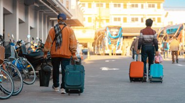Günlük giysiler içinde bavul taşıyan yaşlı bir gezginin arka görüntüsü. Kıdemli adam sabah bavuluyla sokakta yürüyor. Tatil için bagajı olan bir erkek turist. Tatil ve seyahat kavramı.