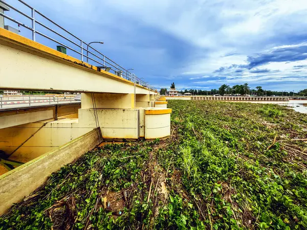 stock image View of irrigation canal with weeds and debris flowing together with strong flowing dirty brown water due to soil and mud from forest after heavy rains and floods. La Nina crisis, Water pollution.