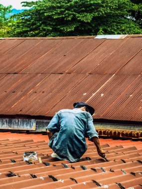 Teknisyen çatıdaki sızıntıyı kapatmak için poliüretan kullanıyor. Adam yağmur sızıntılarını kapatmak için dolgu macunu sürerek çatıyı onardı. İşçi eski kiremit çatısını onarmak için su geçirmez çatı kaplaması kullanıyor..