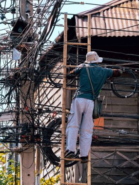 Elektrikçi, eski bir ahşap köyde elektrik sistemini onarmak için merdivenin üzerinde duruyor. Elektrik direklerine bağlı fiber optik kablolar için merdivende çalışan teknisyen..