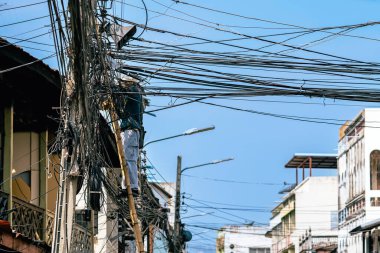 Elektrikçi, eski bir ahşap köyde elektrik sistemini onarmak için merdivenin üzerinde duruyor. Elektrik direklerine bağlı fiber optik kablolar için merdivende çalışan teknisyen..