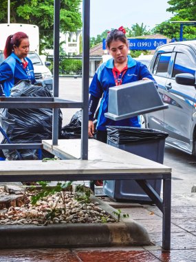 KANCHANABURI, THAILAND-11 Temmuz 2024: Kimliği belirlenemeyen Asyalı kadın işçiler çöp torbalarıyla çöp topluyorlar. İki kadın işçi çöp torbasını temizlemek için çöp torbasına çeviriyor..